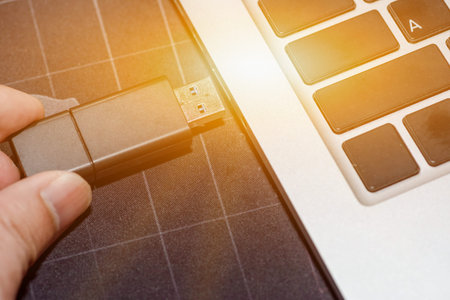 Hand inserting USB flash memory drive plugged into a computer laptop port.
