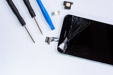 The smartphone was damaged and needs repair. Tools are present that stand isolated on a white background by the hands of a repairman.の写真素材