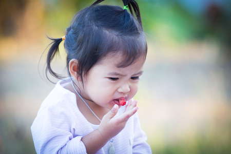 Cute little girl is eating mulberry with sour feelingの写真素材