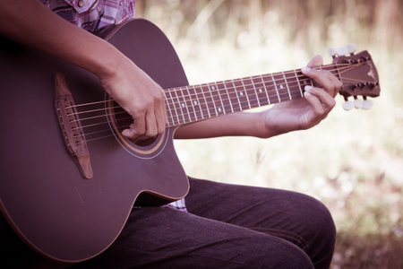 Male hand playing acoustic guitar on meadow background in retro style
