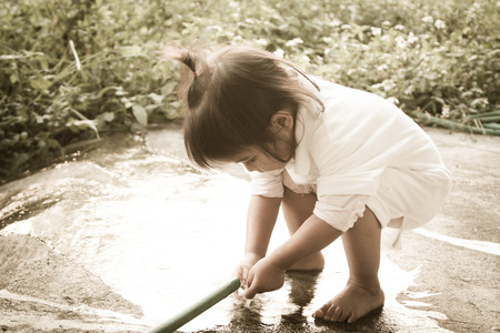 Cute little girl is washing her hand with rubber tube in vintage styleの写真素材