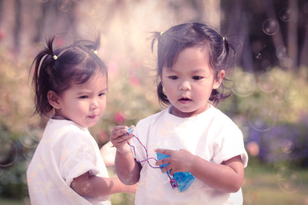Cute little girls playing  bubble together in the flower garden