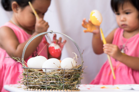 Egg on basket on two little girls painting easter egg backgroundの写真素材