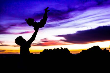 Silhouette of father holding little girl on a beach at sunsetの写真素材