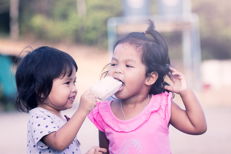 two little girls having fun to eat icecream together,vintage color filterの写真素材