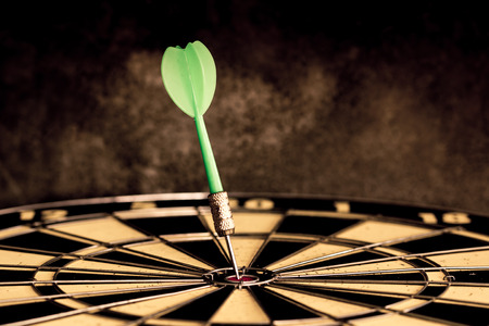 Success hitting target aim goal achievement. Dart in target center on dartboard, vintage effect filter