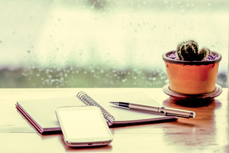 Phone with pen on notebook on rainy day window background in vintage color tone Phone with pen on notebook on rainy day window background in vintage color tone