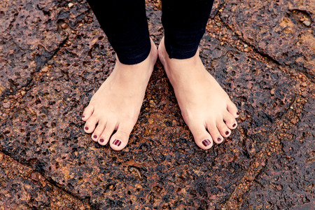 Woman bare feet on wet rocky pavement after rainの写真素材
