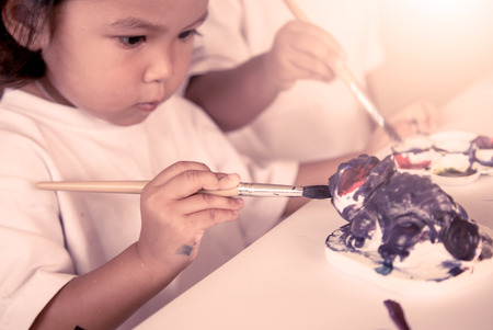 Child painting, little girl having fun to paint on stucco doll in vintage filter,selective focus on hand holding paintbrushの写真素材