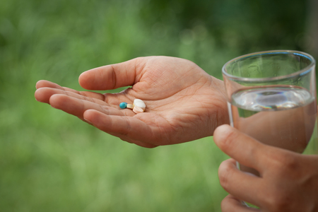 woman hand holding heap of pills and water glass in green nature backgroundの写真素材