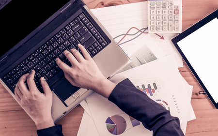 Businesswoman hand typing on laptop keyboard and analyzing business report, working over wooden desk in office in vintage color filterの写真素材