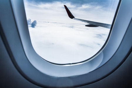 airplane wing and cloudscape seen through airplane window from the passenger seat in blue color filterの写真素材