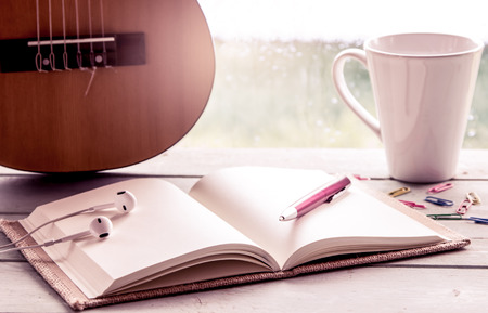 Pen on open notebook on guitar and coffee cup in rainy day window background, vintage filterの写真素材