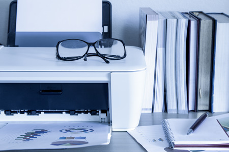 eyeglasses on printer with books on wooden table,blue color toneの写真素材