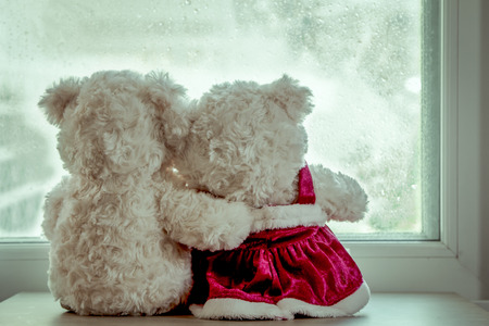 Couple teddy bears in love's embrace sitting in front of a rainy day window,vintage filterの写真素材