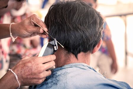 Old man having a haircut with a hair clippers in barber shop in vintage color filterの写真素材