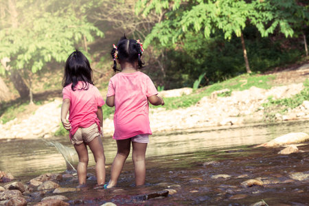 Child two girls having fun to play in waterfall together in summer time,vintage color filter