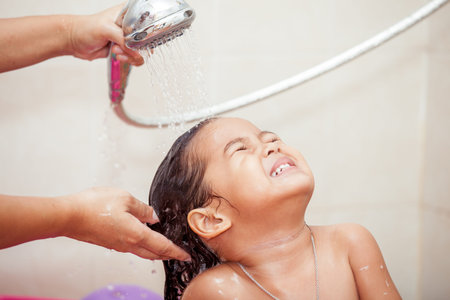 Mother's hand pours water from shower to wash little girl's hair
