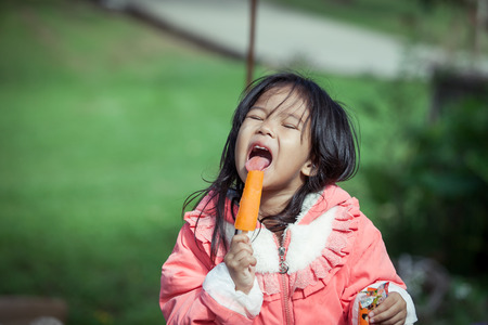 Cute asian little girl is eating ice-cream in the parkの写真素材