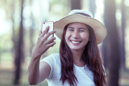 Young asian woman put on hat and  taking selfie on mobile phone in the park in vintage color toneの写真素材