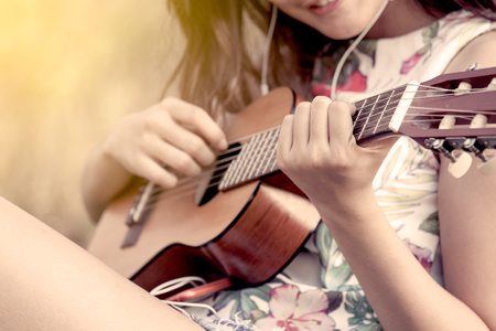 Young asian woman playing acoustic guitalele in the park in vintage color toneの写真素材