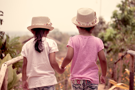 Back view of two little girls holding hand and walking together in the garden in vintage color toneの写真素材