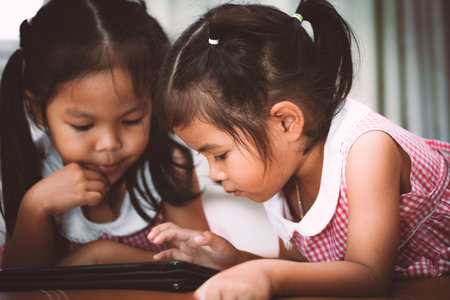 Two asian little girls having fun to watch on tablet together in vintage color toneの写真素材