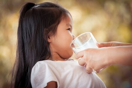 Mother try to give a glass of milk to asian little girl she don't like itの写真素材