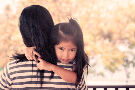 Mother and child cute little girl resting on her mother's shoulder in vintage color toneの写真素材