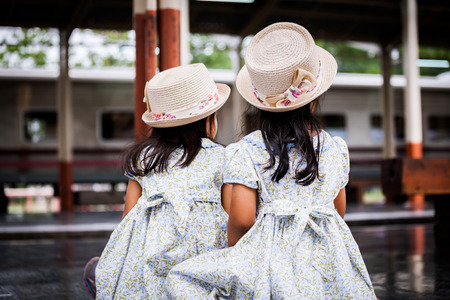 Back view of two cute asian little girls waiting for the train  together on a railway station in vintage retro styleの写真素材