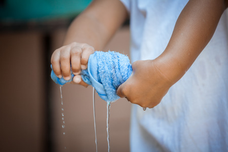Child hands squeeze wet blue towel and water dropの写真素材