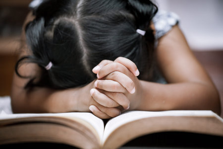 Little girl hands folded in prayer on a Holy Bible in church  for faith concept in vintage color toneの写真素材