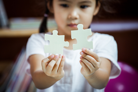 Cute asian little girl is trying to connect couple jigsaw puzzle piece to learn to find solutionの写真素材