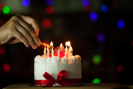 Woman hand lighting candle on birthday cake in dark toneの写真素材
