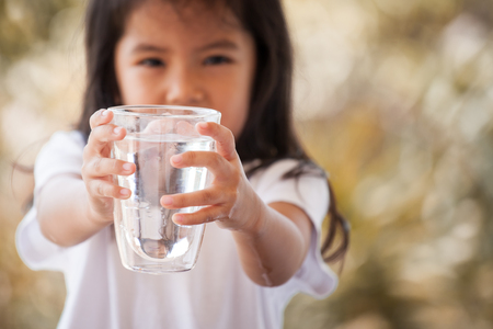Cute asian little girl holding glass of fresh water in vintage color toneの写真素材