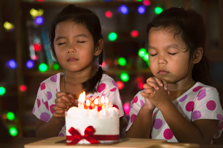 Happy twin two asian little girls make folded hand to wish the good things for their birthday in birthday party in dark toneの写真素材