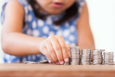 Cute asian little girl playing with coins making stacks of money,kid saving money for the future conceptの写真素材