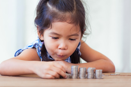 Cute asian little girl playing with coins making stacks of money,kid saving money for the future conceptの写真素材