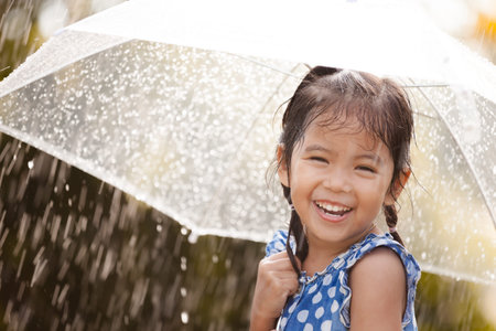Happy asian little girl with umbrella in rain in vintage color toneの写真素材