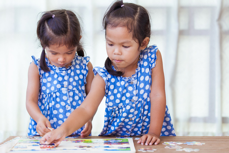 Two children hands helping and trying to connect jigsaw puzzle piece to learn to find solutionの写真素材