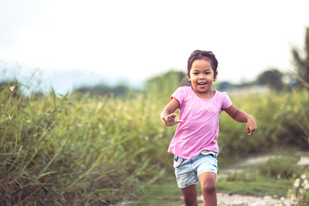 Cute asian little girl having fun and running in the park in vintage color toneの写真素材