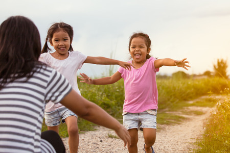 Two asian little girls running to their mother to give a hug in the park in vintage color toneの写真素材