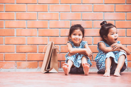 Two Asian girls who feel bored sitting and hugging their knees on the floor while waiting for their...