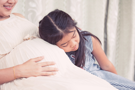 Asian child girl  listening baby in pregnant mother's  belly with love waiting for new baby sisterの写真素材
