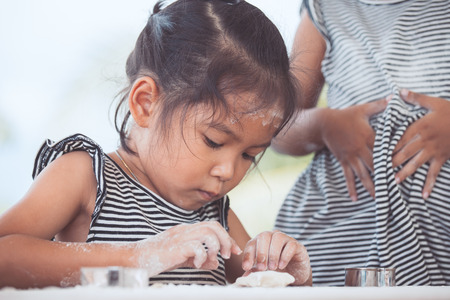 Cute asian little child girl prepares a dough for baking cookies in the kitchen in vintage color toneの写真素材