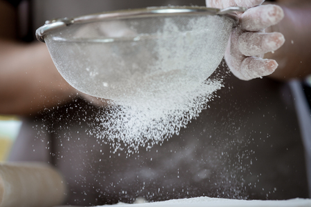 Woman prepare bread dough, spreading the flour through a sieve on dough for baking cookies in the kitchen in vintage color toneの写真素材