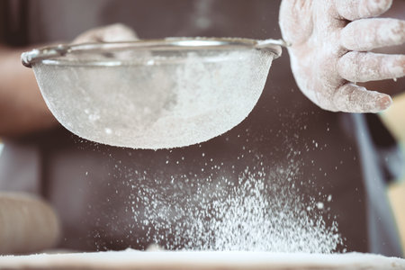 Woman prepare bread dough, spreading the flour through a sieve on dough for baking cookies in the kitchen in vintage color toneの写真素材