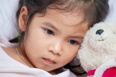 Cute asian little child girl with her teddy bear and lying in bed with sad moody at homeの写真素材