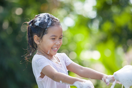 Happy asian child girl having fun to bath and play with foam in outsideの写真素材