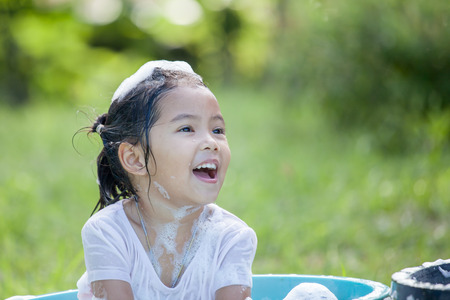 Happy asian child girl having fun to bath and play with foam in outsideの写真素材